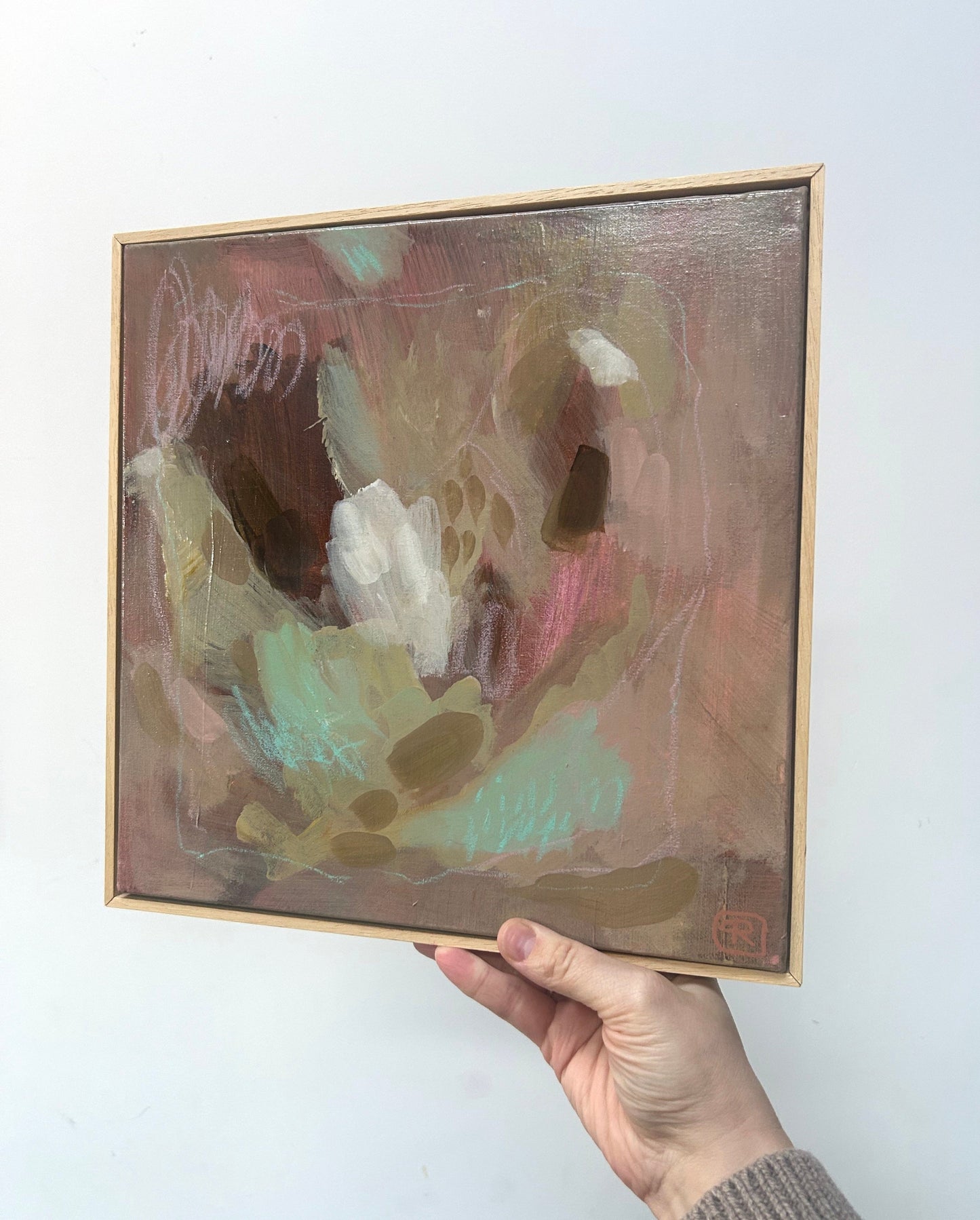 Abstract earthy tones original painting by Ruta Puidokaite held by a hand against a white wall.