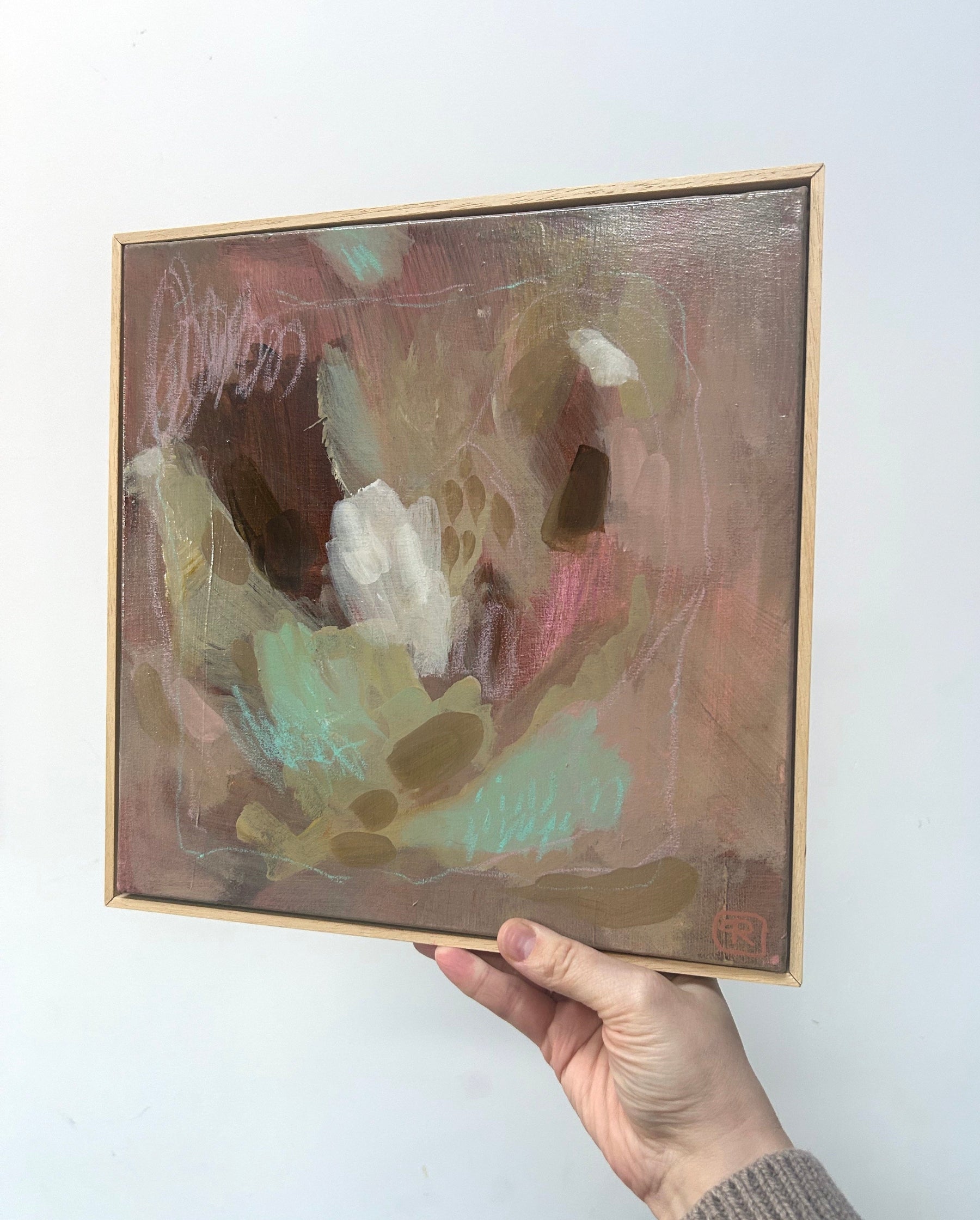 Abstract earthy tones original painting by Ruta Puidokaite held by a hand against a white wall.